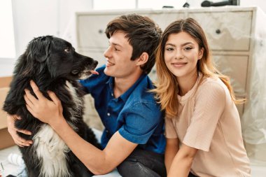 Genç beyaz çift mutlu bir şekilde gülümsüyor. Yeni evlerinde yerde köpekleriyle oturuyorlar..