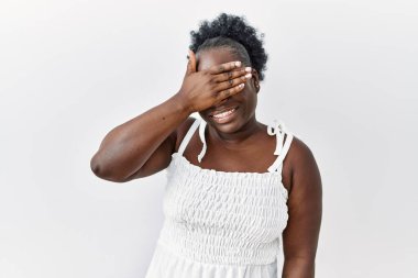 Genç Afrikalı bir kadın izole edilmiş beyaz arka planda duruyor. Gülümsüyor ve gülümsüyor. Gözleri şaşkınlıkla örtüyor. kör kavram. 