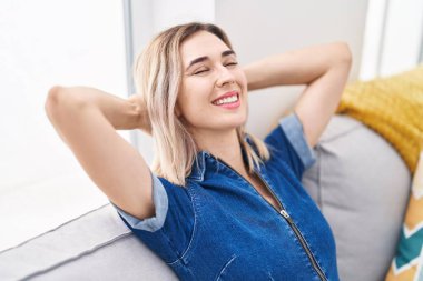 Young woman relaxed with hands on head sitting on sofa at home