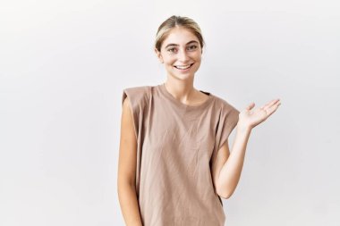 İzole edilmiş arka planda duran genç sarışın kadın mutlu bir şekilde sunum yapıyor ve avuç içiyle kameraya bakıyor.. 