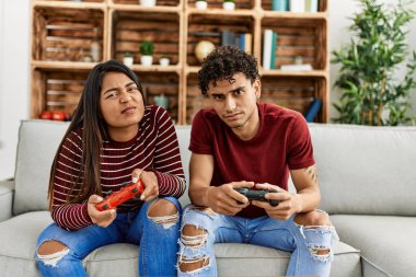 Young latin couple unhappy playing video game sitting on the sofa at home.