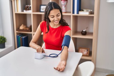Genç Afro-Amerikalı kadın evde masada otururken tansiyon ölçer kullanıyor.