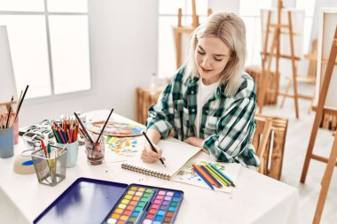 Sanat stüdyosundaki masada oturmuş mutlu bir şekilde gülümseyen genç sanatçı kız..