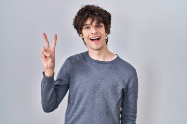 Young man standing over isolated background showing and pointing up with fingers number two while smiling confident and happy. 