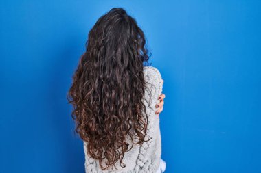 Genç esmer kadın mavi arka planda dikilip kendine sarılıyor mutlu ve pozitif bir şekilde. Sevgi ve özgüven. 