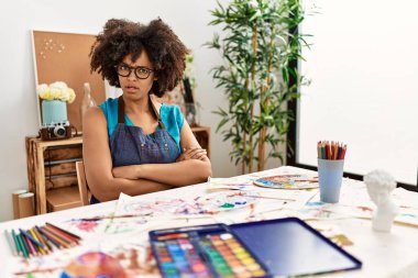 Güzel Afro saçlı Amerikalı kadın sanat stüdyosunda resim yapıyor. Şüpheci ve gergin. Yüzünde çapraz kollarla onaylamayan bir ifade var. negatif kişi. 