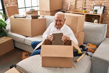 Senior man smiling confident unboxing package at new home