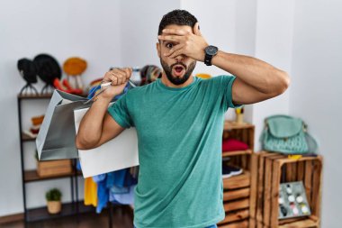 Satış mağazasında sakallı genç yakışıklı bir adam. Şok olmuş bir şekilde yüzünü ve gözlerini kapatıyor. Utanmış bir ifadeyle parmaklarının arasından bakıyor.. 