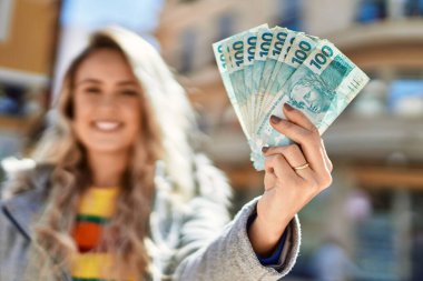 Elinde Brezilya parası olan gülümseyen genç sarışın kadın.