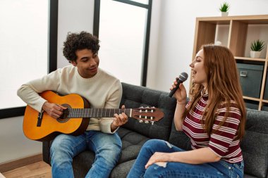 Genç çift klasik gitar çalıyor ve evde mikrofon kullanarak şarkı söylüyor..