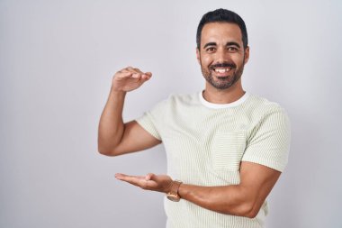 İzole edilmiş arka planda duran sakallı İspanyol bir adam. Elleri büyük ve büyük boy işareti gösteriyor. Ölçü sembolü. Kameraya bakıp gülümsüyor. ölçüm kavramı. 