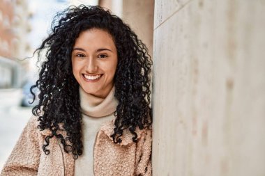 Young hispanic woman smiling confident leaning on the wall at street