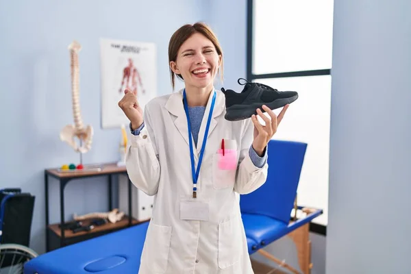 Young Physiotherapist Woman Holding Sneakers Screaming Proud Celebrating Victory Success — Fotografia de Stock