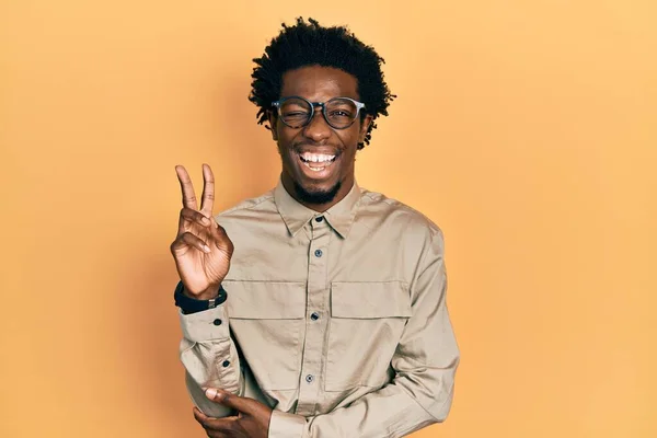 カジュアルな服を着た若いアフリカ系アメリカ人の男性と カメラが勝利サインをするのを見て微笑むグラス — ストック写真