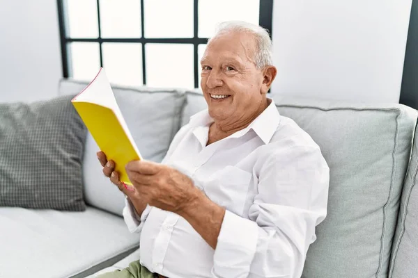 Senior man reading book sitting on sofa at home
