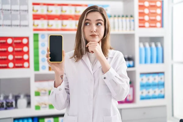 Blonde Caucasian Woman Working Pharmacy Drugstore Showing Smartphone Screen Serious — Foto Stock