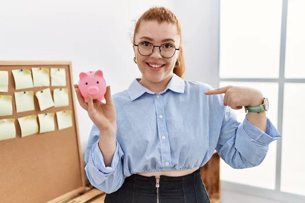 Ung Rödhårig Kvinna Håller Spargris Bank Kontoret Pekar Finger Till — Stockfoto