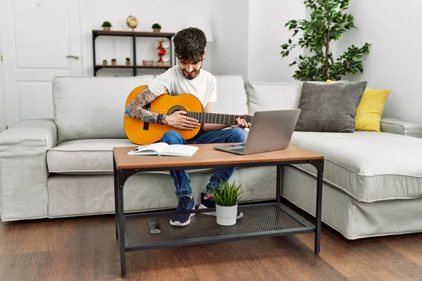 Ung Latinamerikansk Man Spelar Klassisk Gitarr Och Använder Laptop Hemma — Stockfoto