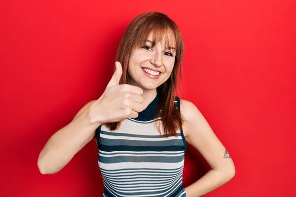 红头发的年轻女人穿着休闲的T恤 手拿着快乐的大拇指做手势 赞成的表情看着相机显示的成功 — 图库照片