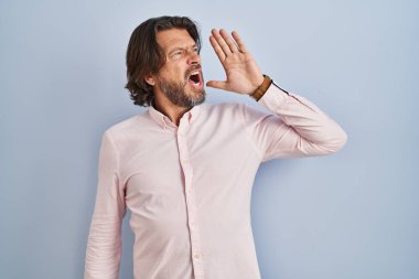 Handsome middle age man wearing elegant shirt background shouting and screaming loud to side with hand on mouth. communication concept. 