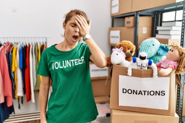 Beautiful caucasian woman wearing volunteer t shirt at donations stand yawning tired covering half face, eye and mouth with hand. face hurts in pain. 