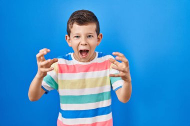 Mavi arka planda dikilen genç beyaz çocuk öfkeden kudurmuş, elleri boğazlamaya çalışıyor, deli gibi bağırıyor. 