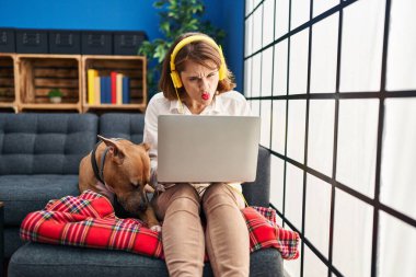 Young beautiful woman using laptop sitting on the sofa pointing with finger to the camera and to you, confident gesture looking serious 