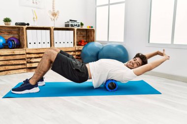 Genç İspanyol adam klinikte köpük silindiri kullanarak rehabilitasyon yapıyor.