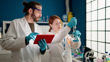 Laboratuvarda dokunmatik ped kullanan bilim adamı ve kadın üniforması giyiyor.