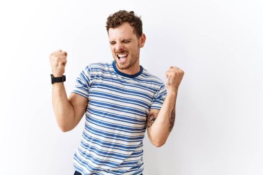 Tecrit edilmiş arka planda duran yakışıklı genç adam şaşırmış ve şaşırmış bir şekilde kollarını kaldırmış ve gözlerini kapatmış bir şekilde başarıyı kutluyor. Kazanan konsept. 