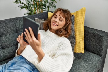 Beyaz bir kadın dokunmatik ped kullanıyor. Evdeki kanepede yatıyor.