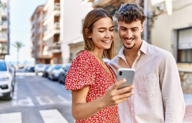 Genç İspanyol çift mutlu bir şekilde gülümsüyor ve şehirde akıllı telefon kullanıyor..