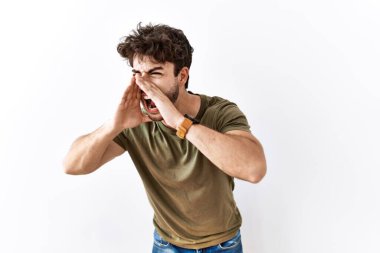 Hispanic man standing over isolated white background shouting angry out loud with hands over mouth 