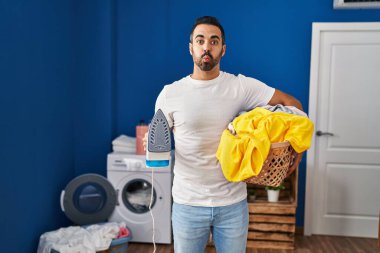 Sakallı, sakallı, elinde ütü ve komik suratlı, evde tüten yanakları olan genç İspanyol bir adam. Ağzı havayla şişer, havayı yakalar.. 