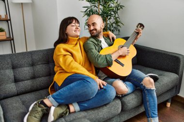Genç İspanyol çift gülümseyerek evde kanepede oturmuş klasik gitar çalıyor..