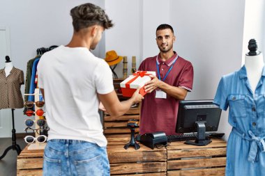 Genç İspanyol esnaf gülümseyerek giyim mağazasındaki müşteriye hediye veriyor..