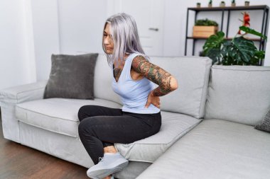 Orta yaşlı, kır saçlı, sırtı ağrıyan kadın evdeki kanepede oturuyor.