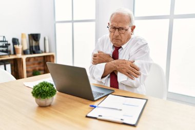Senior man working at the office using computer laptop shaking and freezing for winter cold with sad and shock expression on face 