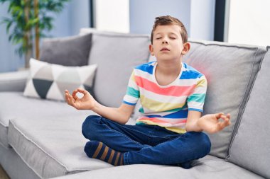 Sarışın çocuk evdeki kanepede yoga egzersizi yapıyor.