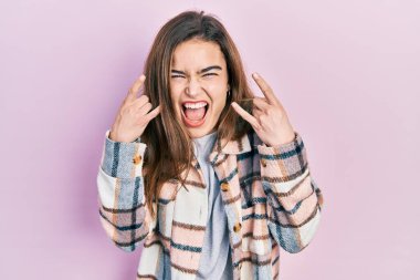 Günlük kıyafetler giymiş, çılgın bir ifadeyle bağıran beyaz bir kız elleri havada rock sembolü yapıyor. Müzik yıldızı. ağır müzik konsepti. 