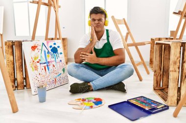 Sanat stüdyosundaki genç İspanyol adam diş ağrısı ya da diş hastalığından dolayı acı dolu bir ifadeyle ağıza dokunuyor. dişçi 