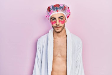 Bornoz ve duş başlığı takan genç İspanyol adam göz torbaları takıyor. Düşünce biçimi ve kendine güvenen ayık yüz ifadesi takınıyor. 