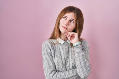 Güzel bir kadın pembe arka planda, elleri çenesinde soru sorarken, düşünceli bir ifade takınıyor. Düşünceli bir yüzle gülümsüyor. şüphe kavramı. 
