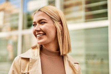 Genç sarışın kız gülümsüyor, mutlu bir şekilde şehirde duruyor..