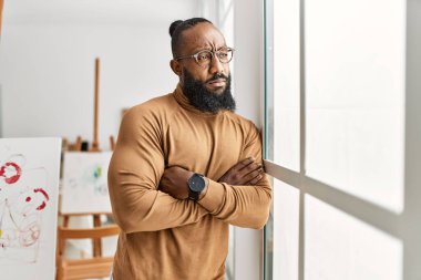 Ciddi bir ifadeyle genç Afrikalı Amerikalı sanatçı sanat stüdyosunda kollarını kavuşturmuş duruyor..