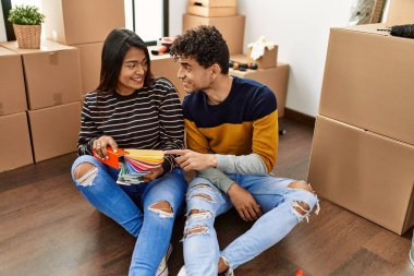 Young latin couple choosing paint color sitting on the floor at new home.