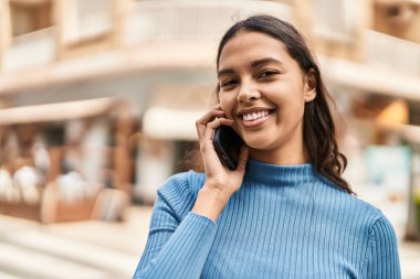Genç Afrikalı Amerikalı kadın gülümsüyor. Kendine güveni tam. Sokakta akıllı telefondan konuşuyor.