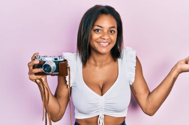 Young african american girl holding vintage camera screaming proud, celebrating victory and success very excited with raised arm 