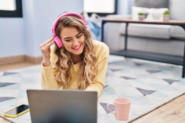 Young woman using laptop and headphones lying on floor at home