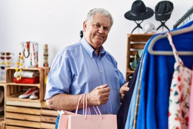 Orta yaşlı, gri saçlı, gülümseyen, kendine güvenen bir adam giyim mağazasından alışveriş yapıyor.